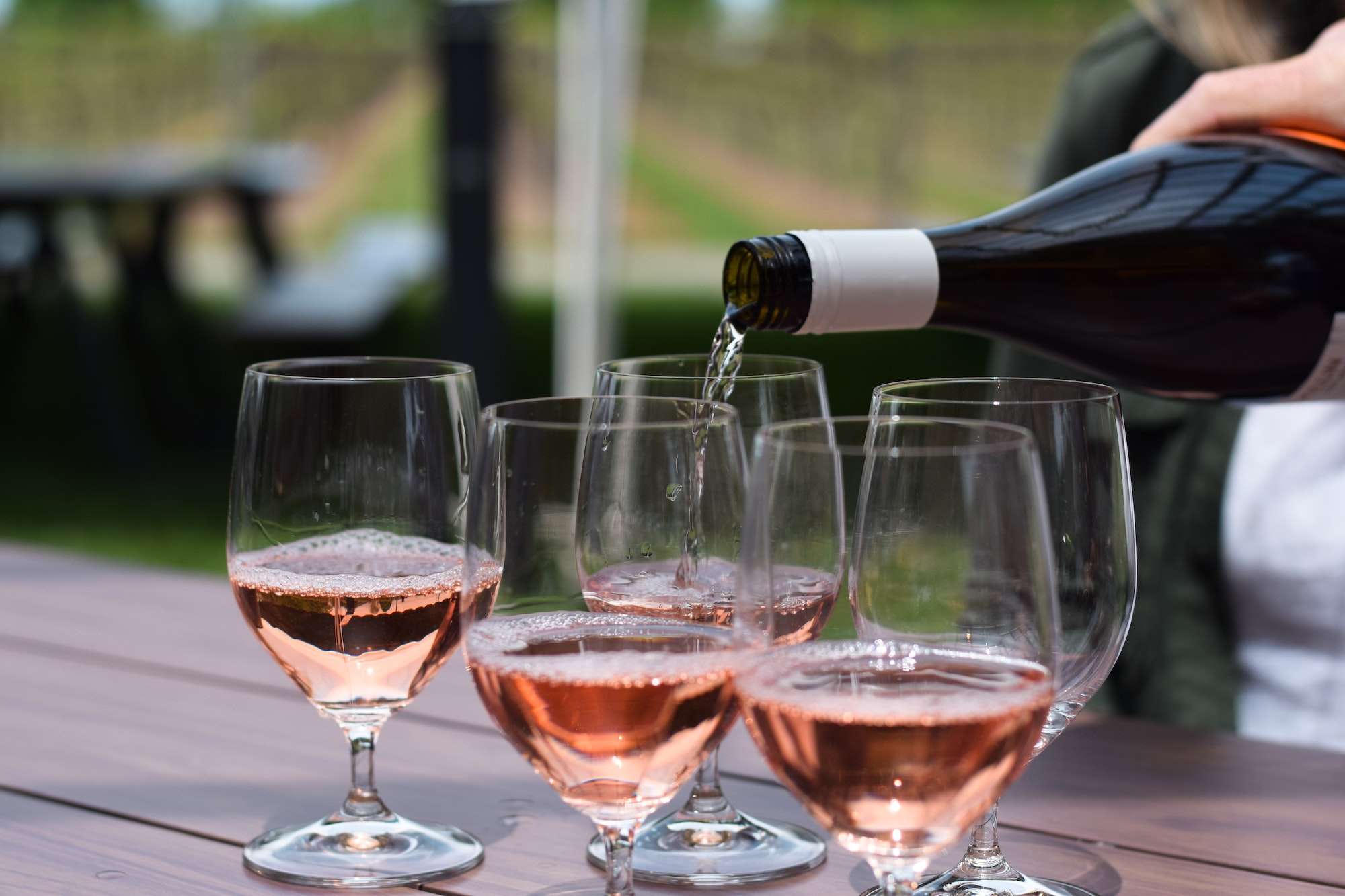 Persons hand pouring rose wine into multiple glasses